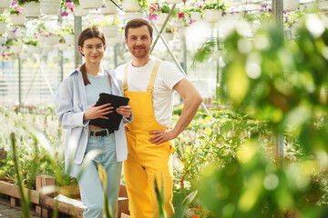 Holding tablet. Florist man and woman are working together in bright greenhouse