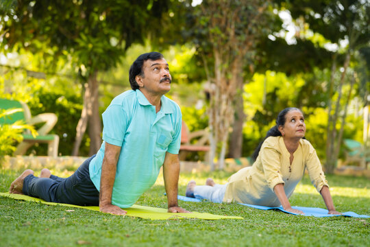Indian healthy senior couple doing yoga or exercising by stretching at park - concept of healthy active lifestyle, wellness and relationship.