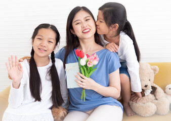 Happy mother's day. Cheerful daughters giving tulip flower and gift to their mom celebrate mother day with love. Cute child hug and kiss her mom with bouquet smiling. Asian family together celebration