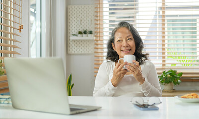 Happy senior woman drinking her morning coffee and looking out of the window.