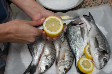 A hand cutting a slice of lemon while cooking fish. Preparing of fresh salt-backed sea fish.