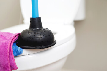 A serviceman is repairing a toilet with a hand plunger caused by a clogged toilet.