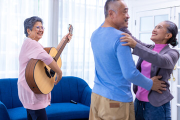 Obraz premium Senior friends on party dancing and playing guitar at home. Elderly musician at party has fun with cheerful family singing together. Leisure activity of Asian Senior.