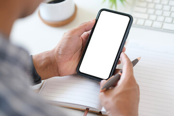 Close up view of man using smartphone at workstation. White empty screen ready for your app.