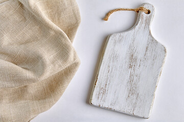A white painted wooden cutting board and a coarse beige linen napkin on a white table