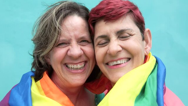 Happy Senior gay lesbian couple having fun wearing Lgbtq rainbow flag at pride parade - Family and love concept