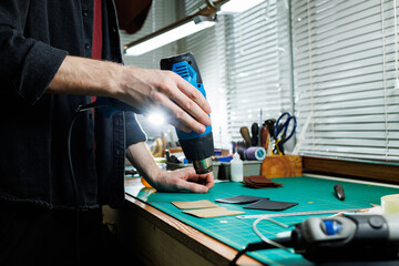 The hands of the master sew handmade leather products. Men's hands connect the parts, creating quality leather accessories. Working process in a leather workshop