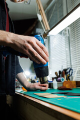The hands of the master sew handmade leather products. Men's hands connect the parts, creating quality leather accessories. Working process in a leather workshop