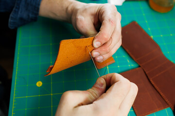 Close-up of the master's hands sewing handmade leather products. A men's tanner connects the parts, creating quality leather accessories. Working process in a leather workshop