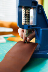 Close-up of the master's hands sewing handmade leather products. A men's tanner connects the parts, creating quality leather accessories. Working process in a leather workshop