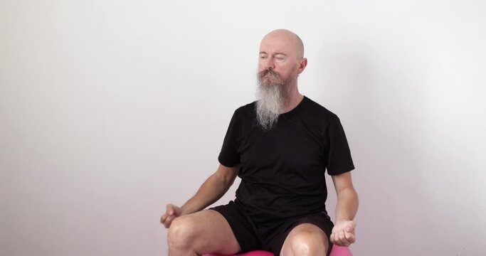 50 year old mid adult man with long beard sitting on fitness ball, doing neck and upper spine exercise at home, pulling hands backwards, real people