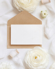 Blank card and envelope near cream roses and white ribbons top view, wedding mockup