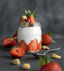 Greek yogurt, nuts and strawberries in a glass jar on grey table with a spoon close up
