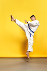Portrait of professional male taekwondo, karate athlete wearing white kimono doing basic movements over yellow background © Lustre Art Group 