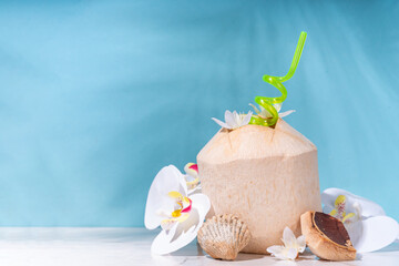  Young Thai coconut cocktail or juice, tropical summer drink in whole young coconut, with tropical leaves, decor and flowers, on high-colored background 
