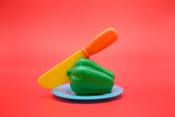 toy green pepper with knife isolated on red background. Mini green pepper that can be attached and removed.