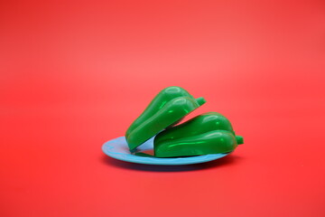 toy green bell pepper on a blue plate isolated on red background. Mini green pepper that can be attached and removed.