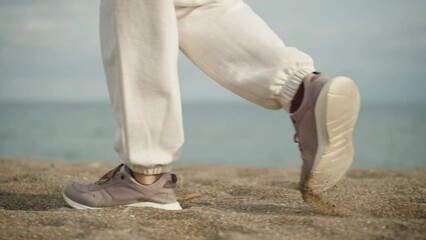 feet in purple sneakers and white pants are walking along a sandy beach along the sea, Cloudy, slow.
