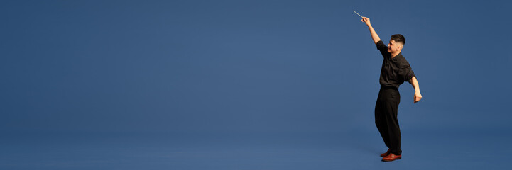 Banner with man, musician wearing costume holding conductor's baton on the stage over dark blue studio background. Copy space for text