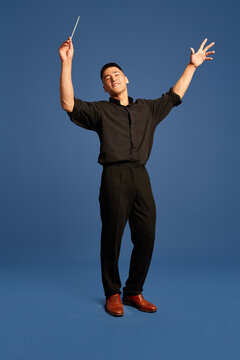 Portrait with one man, musician wearing costume holding conductor's baton on the stage over dark blue studio background. Choral conductor