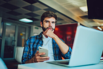 Thoughtful man sitting at table and working on laptop