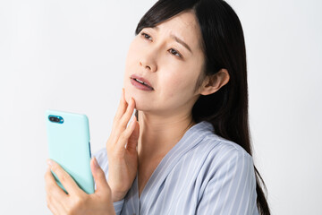 スマートフォンを持ちながらネガティブな表情をする若い女性