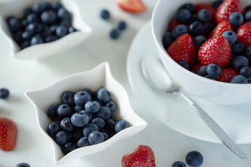 Blueberries and strawberries in white bowls on a white backrgound