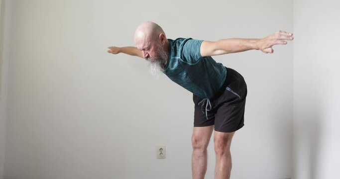 50 year old mid adult man with long beard doing neck and upper spine exercise at home, stretching hands to the left and right side, real people