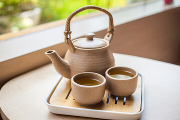 Tea set with kettle and traditional Japanese mugs on a wooden table in the garden.