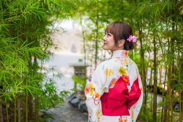 Young woman wearing traditional Japanese kimono or yukata stand with your back in garden with bamboo trees.