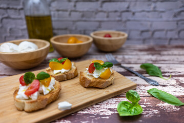Tasty bruschetta with mozzarella, tomato, basil and oil. Background with bokeh effect. Bread on a wooden cutting board.