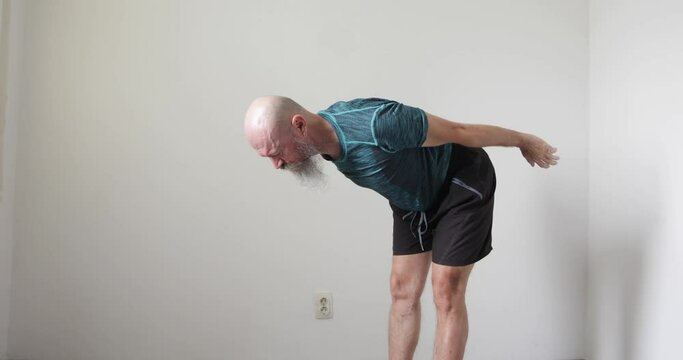 50 year old mid adult man with long beard doing neck and upper spine exercise at home, stretching hands forward and backwards, real people
