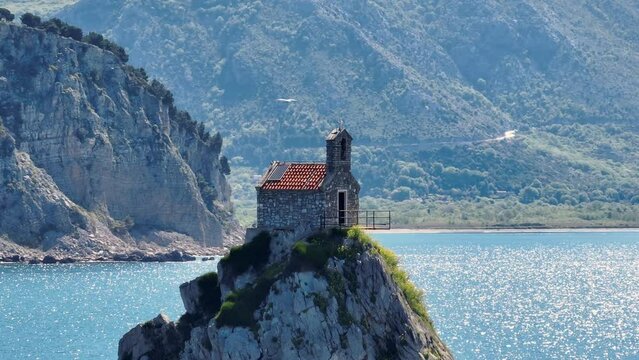 Aerial view church on the stone in the sea in Montenegro, Petrovac city. Seagull fly over in shot. rocky sea shore on a background.telephoto lens shot. Summer sunny day.