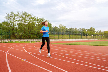 Woman runs on running track in stadium in summer.