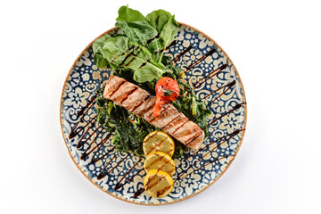 Grilled salmon on a bed of spinach with tomatoes, arugula and lemon