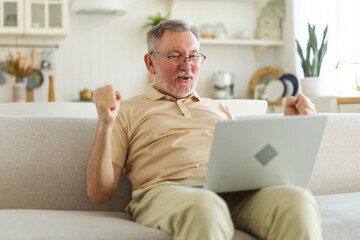 Excited middle aged senior man euphoric winner. Older mature grandfather looking at laptop reading great news getting good result winning online bid feeling amazed. Winning gesture