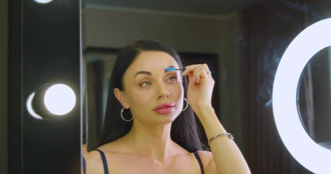 Woman making eyebrow correction in front of a mirror at home.