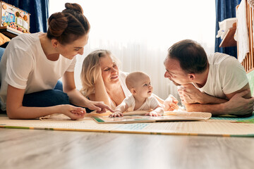 Parents together with their child play and study a children's book, lying on the floor in a bright...