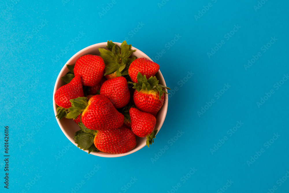 Wall mural Fresh strawberries and green leaf in bowl isolated on blue background,