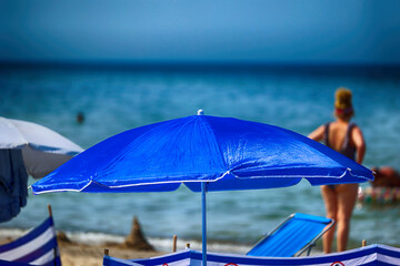 Parasol słoneczny na plaży nadmorskiej w wakacje razem z parawanem na wiatr. - obrazy, fototapety, plakaty