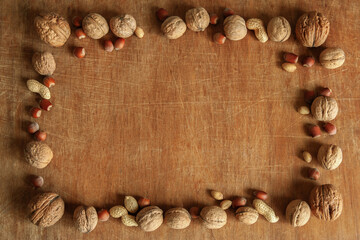 A square frame of different kinds of nuts on an old wooden background.