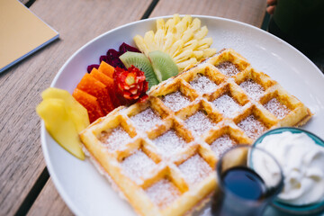 Selective focus on fresh baked Belgian waffles with sugar and ananas for sweet eating in cafe, tasty wafer with cream and exotic fruits during cheat meal weekend leisure in coffee shop