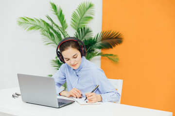 a woman in headphones talks on Skype writes in a notebook Internet remote work online communication