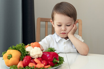 kid doesn't like healthy food concept, sad, unhappy boy next to a dish of fresh vegetables