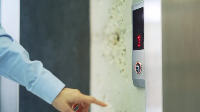 Close up of a woman's hand pressing the elevator call button in a modern office building or hotel. A female in a shirt presses a silver metal button and waits to take the lift to the workplace