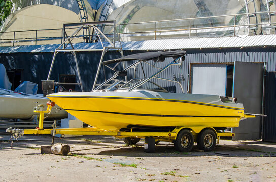 motor boat on boat parking on shore. yellow powerboat on transport trailer is parked next to garage.