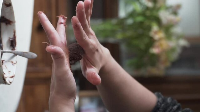 Vertical slow motion video of female hands rolling up brigadero chocolate, close up, natural light