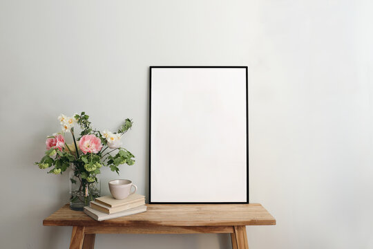 Blank black picture frame mockup. Artistic table, wooden bench still life composition with cup of coffee, old books. Spring bouquett of pink tulips, white daffodils. Hawthorn, guelder rose flowers.