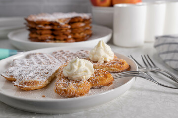 Fresh baked waffles with powdered sugar and whipped cream on kitchen table