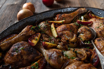 Autumn, winter meat dish with roasted chicken parts, onions and apples. Served in a rustic roasting pan